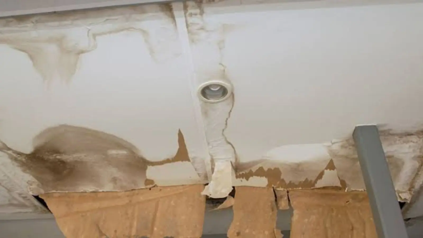 Water-stained ceiling with peeling paint and damaged drywall around a ceiling fixture
