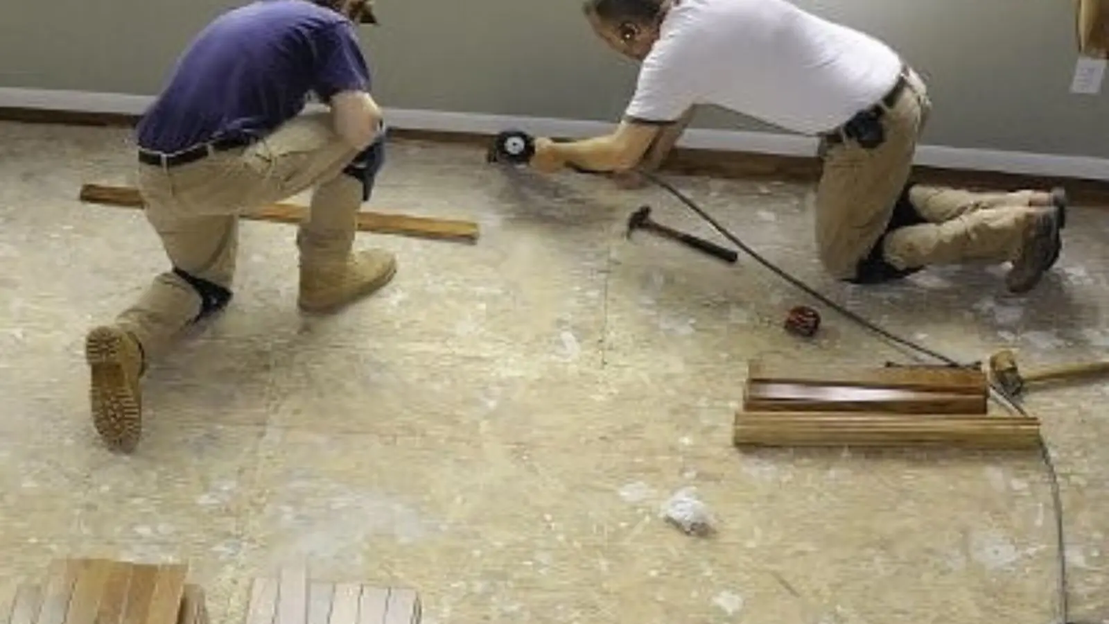 Two workers kneeling on a bare floor measuring and laying out new flooring during water damage repair in Dana Point