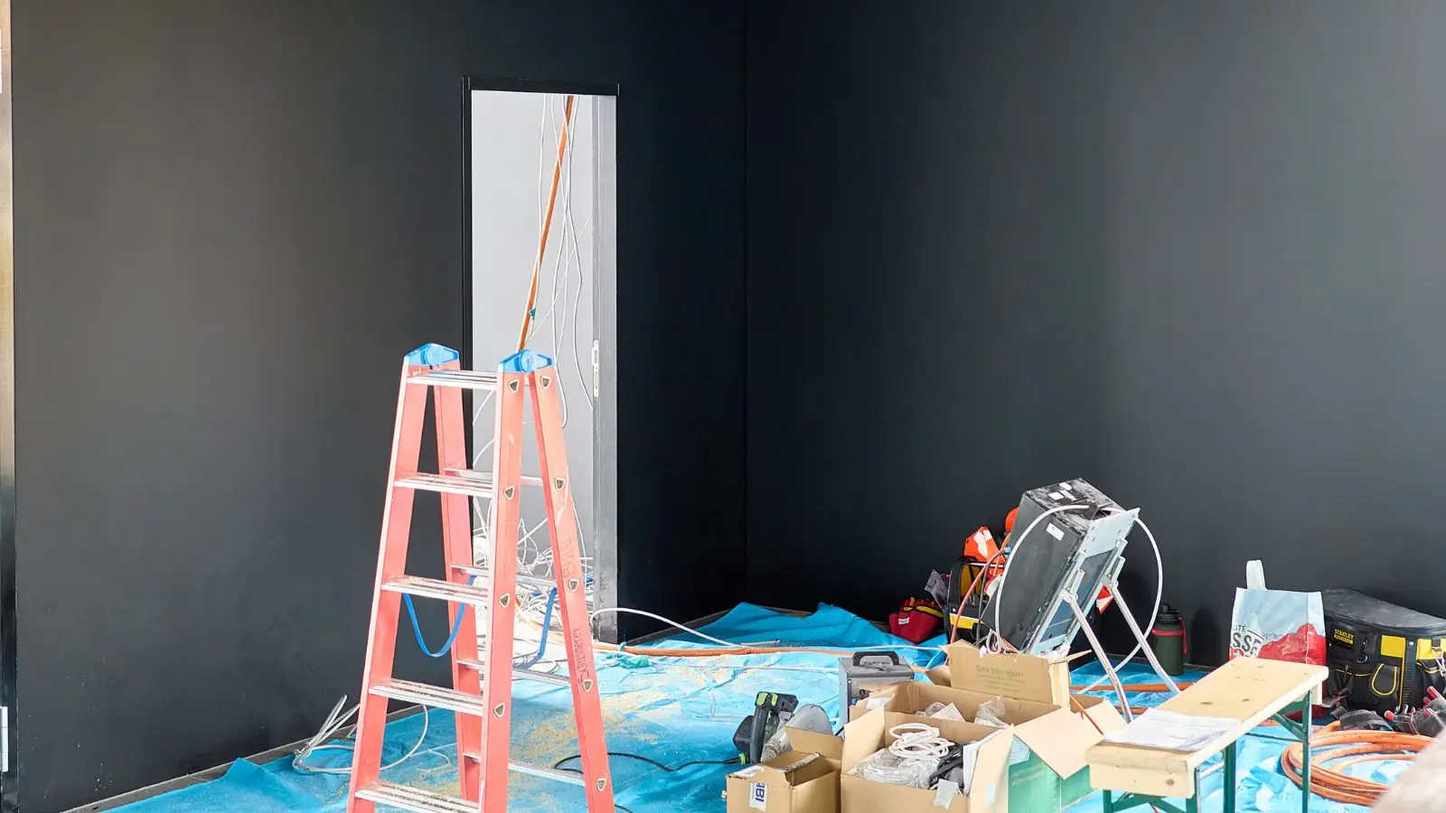 Ladder, tarps and tools in a gutted room during a rebuild after water damage